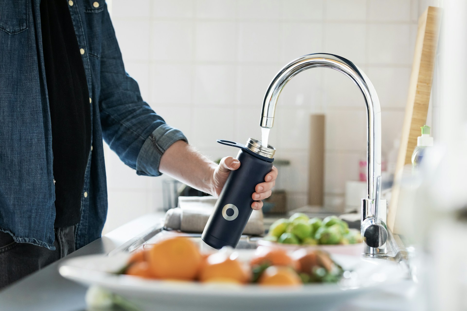 Person filling water bottle from tap at kitchen sink