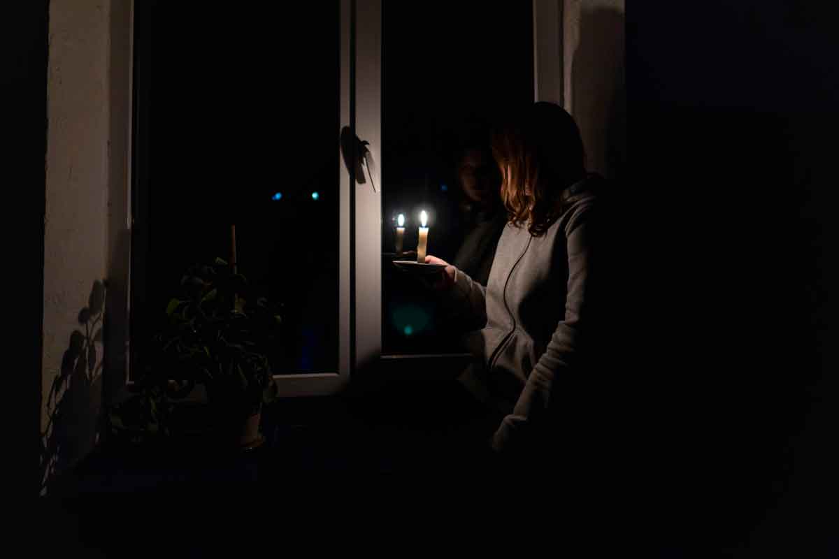 Woman sitting by window lit by a single candle during power outage